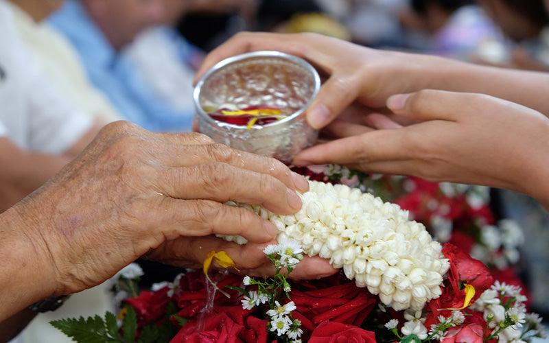 Hands pouring water over an elderly person's floral garland.