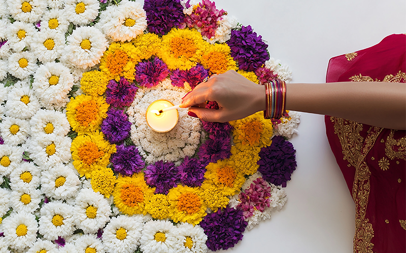 Hand lighting a candle in the center of a floral Deepavali rangoli