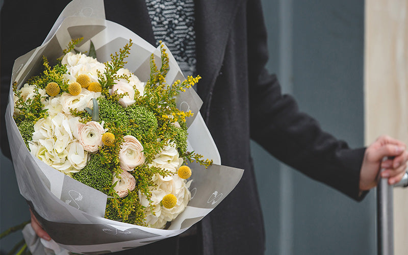 Man holding a fresh white and yellow floral bouquet.
