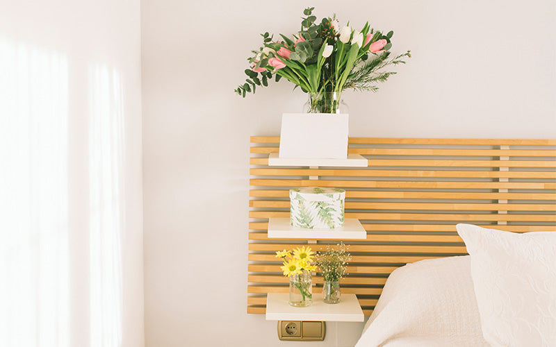 Minimalist bedroom with wooden slatted headboard and three white shelves holding flowers and decor