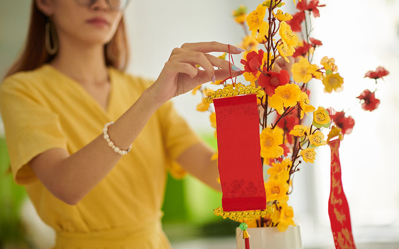 Woman hanging red scroll on Chinese New Year flowers.