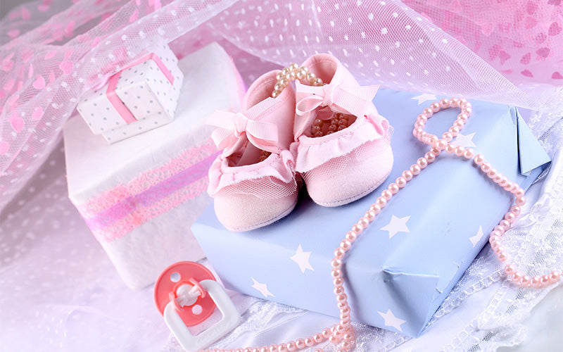 Pink baby shoes and gift boxes for a baby shower.